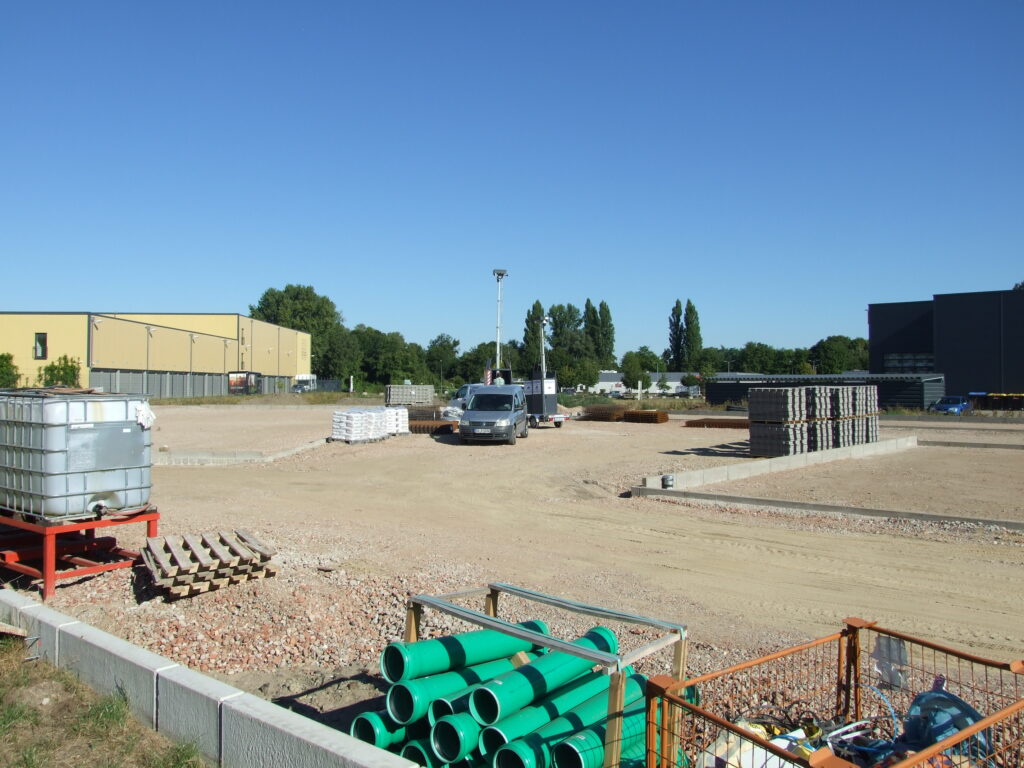 Baustellenbereich mit grünen Rohren und einem großen Betonfundament. Im Hintergrund ist ein ViSec Kameraturm zur Baustellenüberwachung sichtbar, während sich ein Fahrzeug auf der Baustelle befindet.